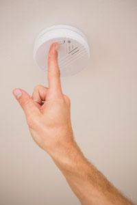 Carbon-Monoxide-Detectors - Picture of a hand testing a smoke detector on the ceiling